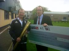 Steve Kingston, men’s team captain, holding the giant cheque, standing with Perry Strung, Olympic torch bearer, who is transforming conditions for cricketers with a disability in Devon.